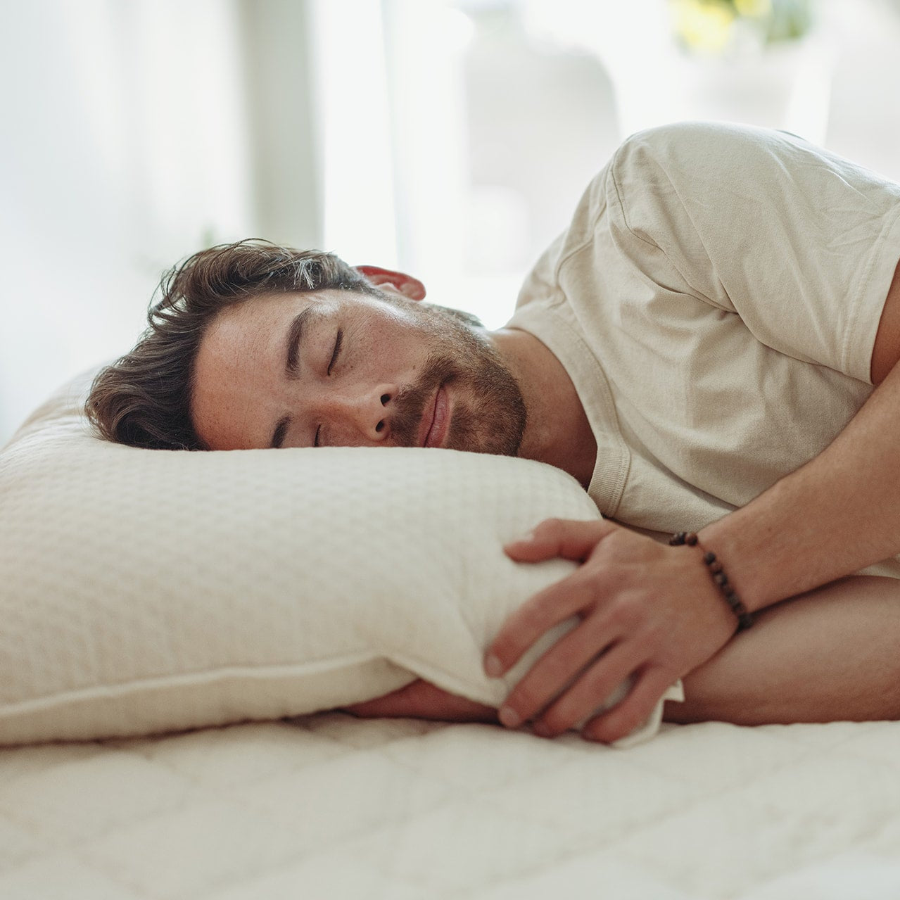 Man lying on a bed with a luxury latex pillow, wearing a white shirt.