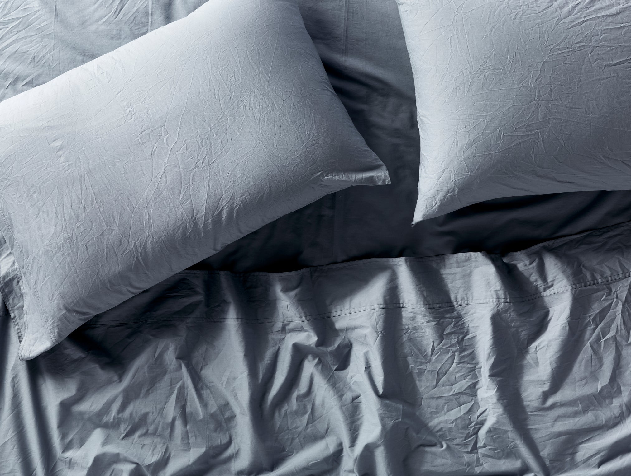 Coyuchi Organic Crinkled Percale Fitted Sheet in Steel Blue – close-up of made bed showing relaxed cotton texture. #colour_steel blue