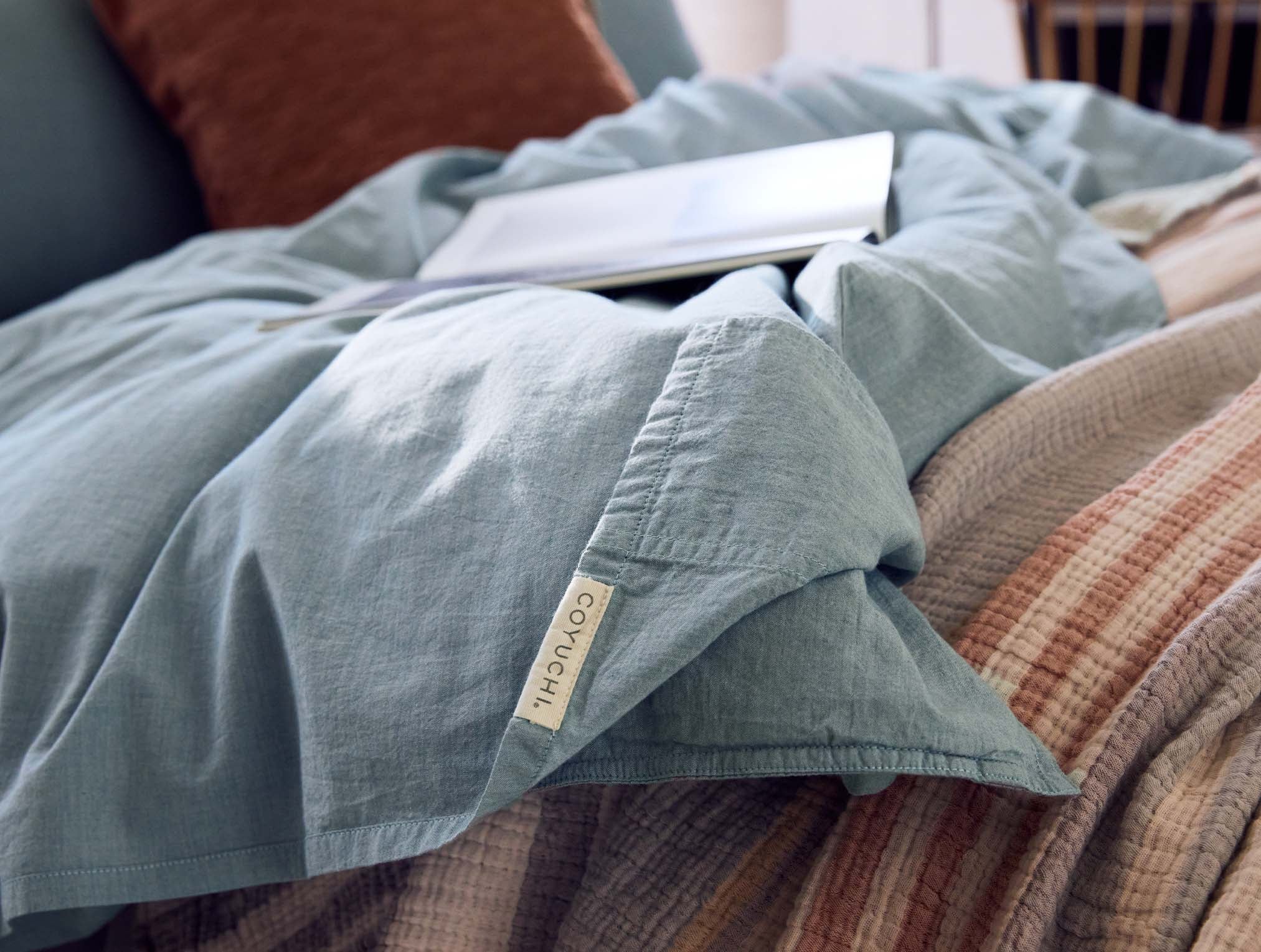 Coyuchi Organic Crinkled Percale Fitted Sheet in Surf Chambray – close-up of seam with logo tag. #colour_surf chambray