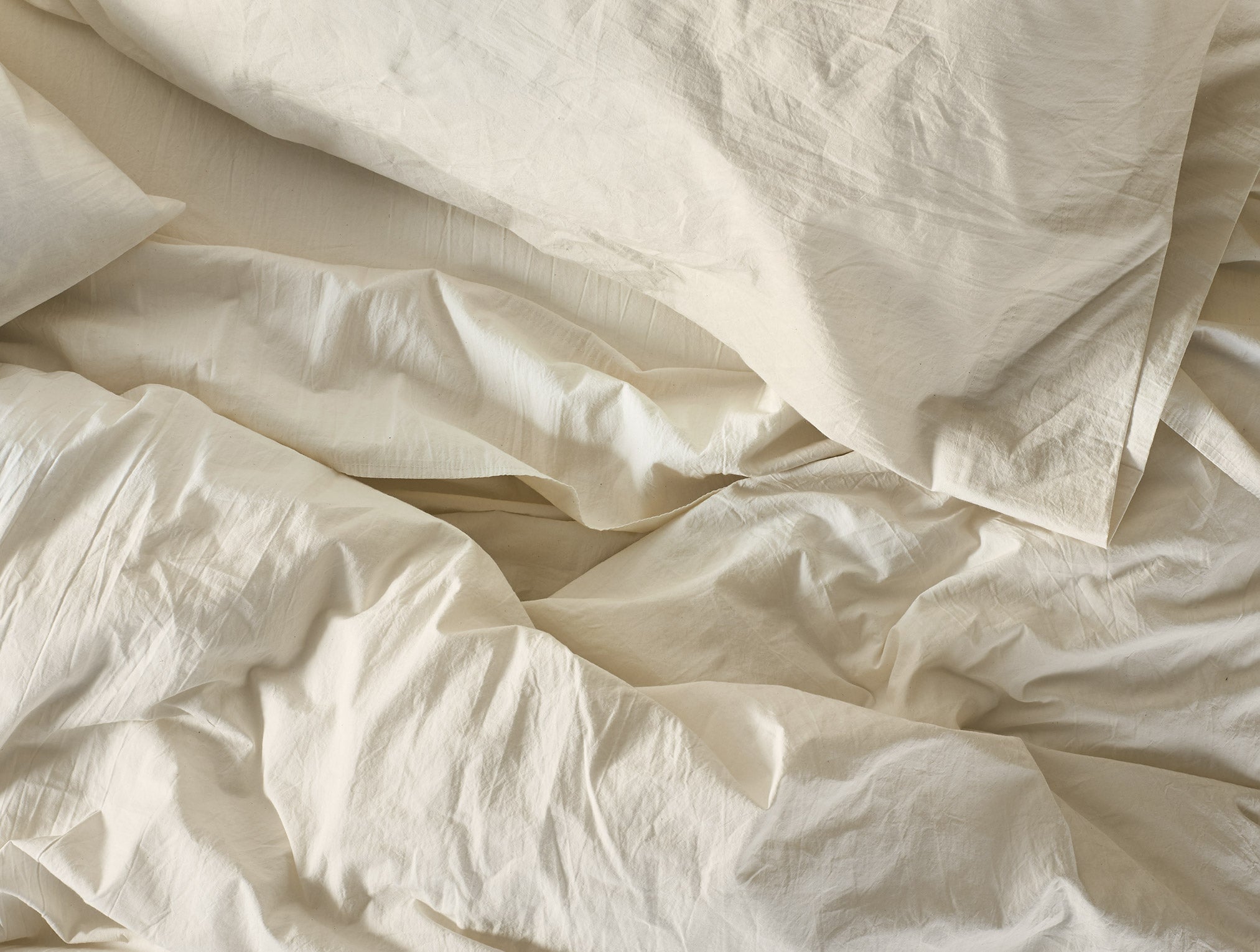 Coyuchi Organic Crinkled Percale Fitted Sheet in Undyed – close-up of made bed showing natural rumpled texture. #colour_undyed
