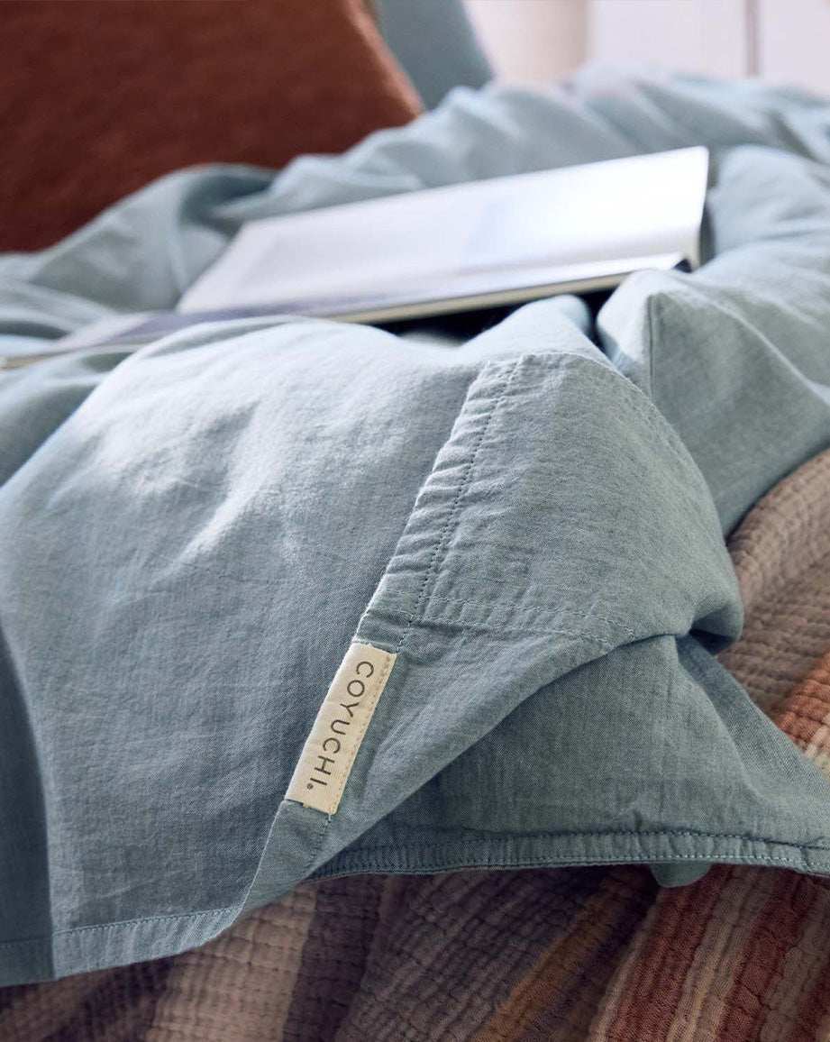 Coyuchi Organic Crinkled Percale Sheet Set in Surf Chambray – close-up highlighting stitching quality and Coyuchi logo. #colour_surf chambray