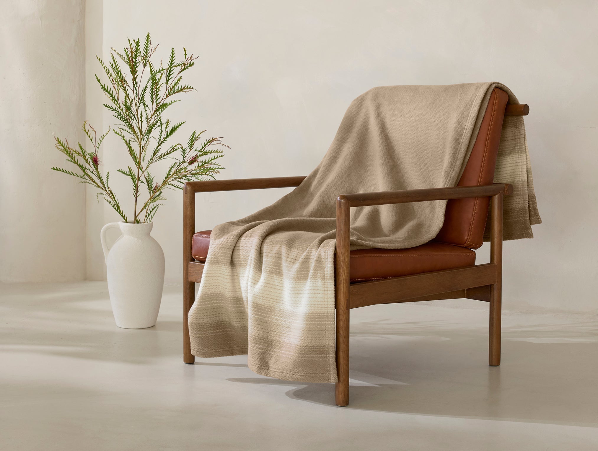 Coyuchi Horizon Supersoft Organic Throw - draped over chair with plant #colour_Camel Ombre