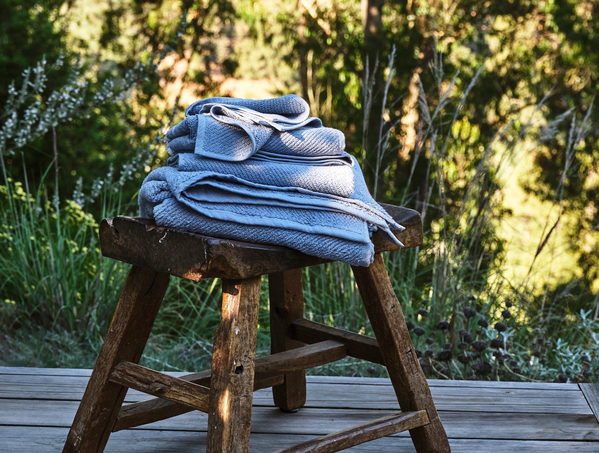 Coyuchi Organic Air Weight Towel - stacked on wooden stool outside #color_stone blue