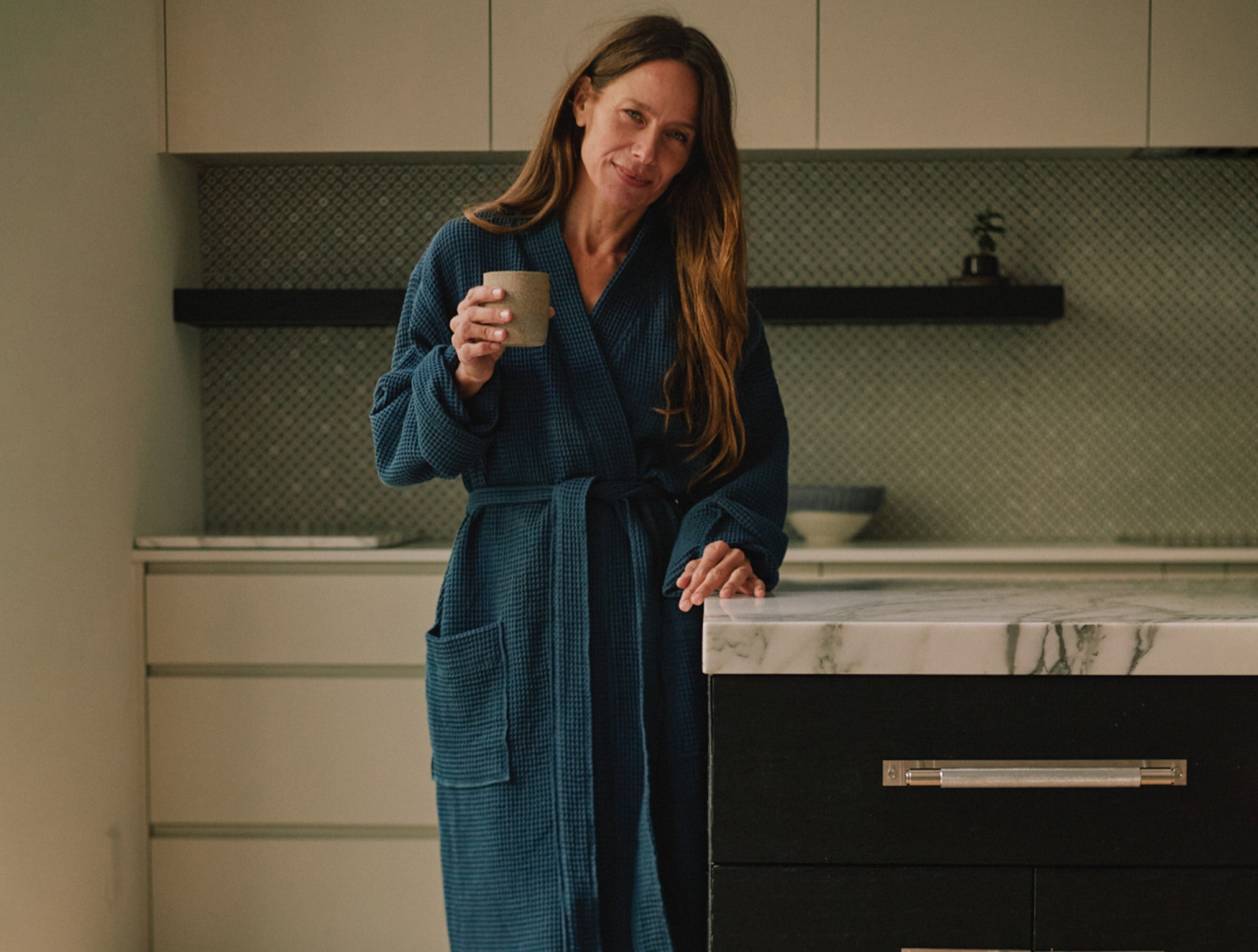 Coyuchi Organic Cotton Unisex Waffle Robe - model holding cup in kitchen #colour_deep ocean