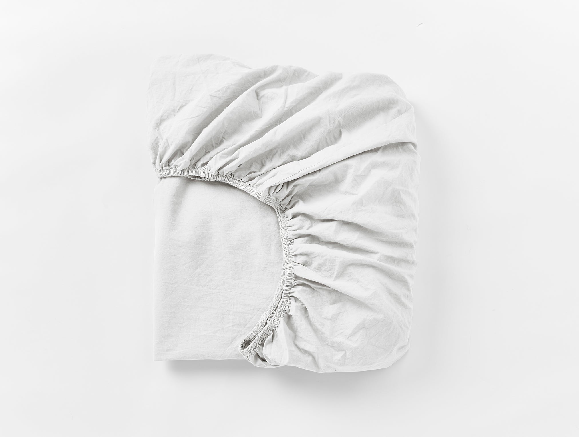 Coyuchi Refined Organic Percale Fitted Sheet in Alpine White – folded, displaying elastic in seam. #colour_alpine white