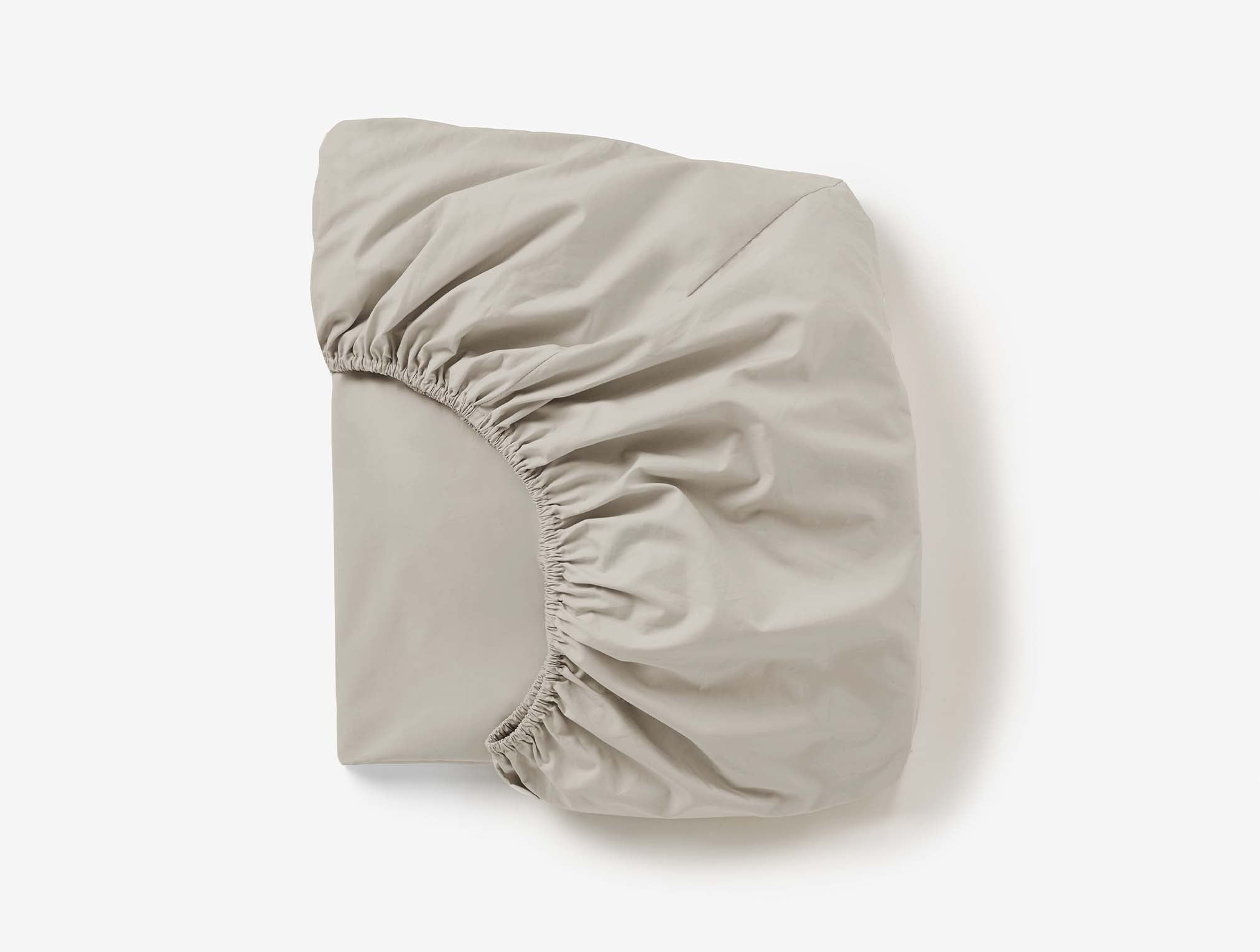 Coyuchi Refined Organic Percale Fitted Sheet in Stone – folded, displaying elastic in seam. #colour_stone