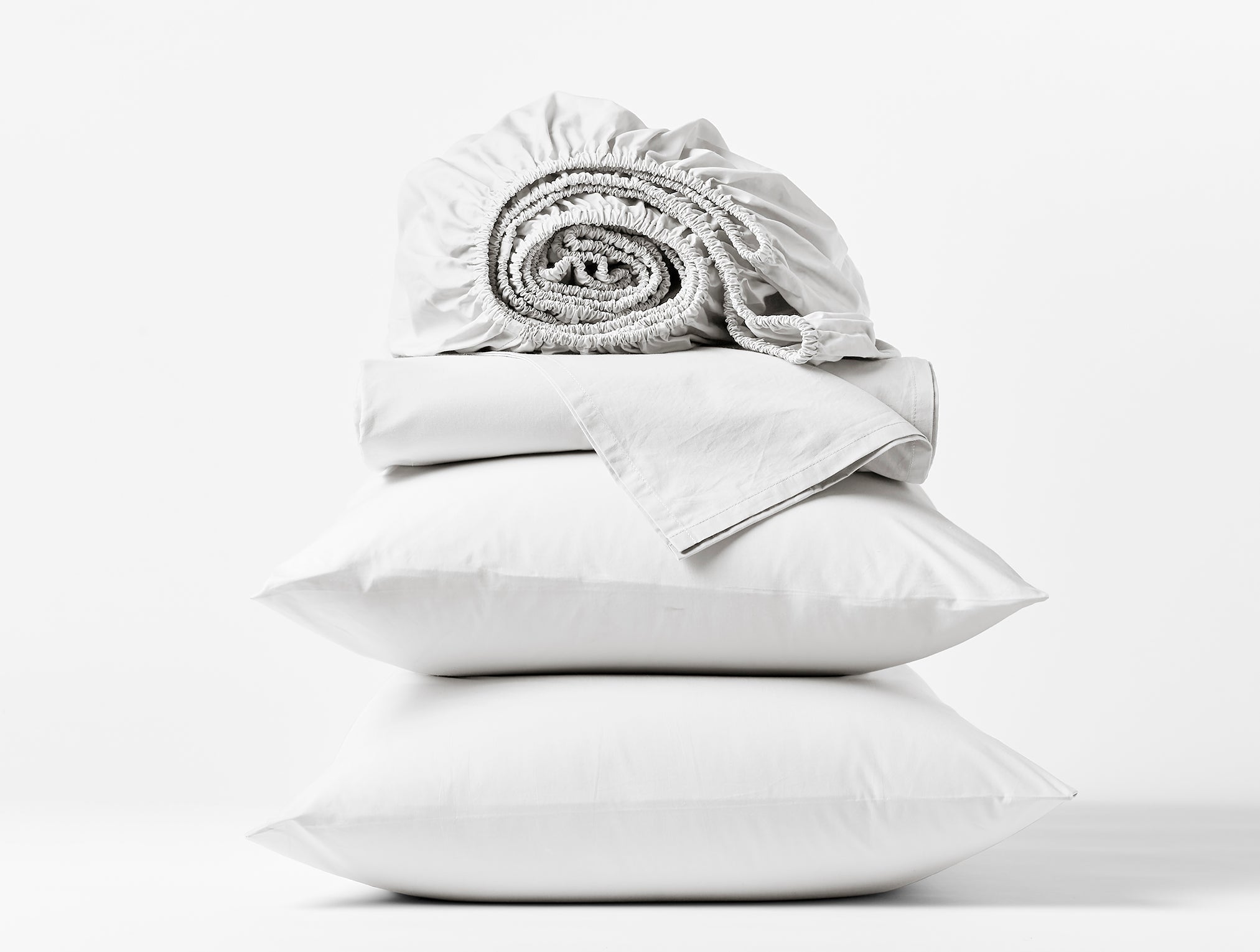 Coyuchi Refined Organic Cotton Percale Sheet Set in Alpine White – stacked display with pillows and folded sheets. #colour_alpine white
