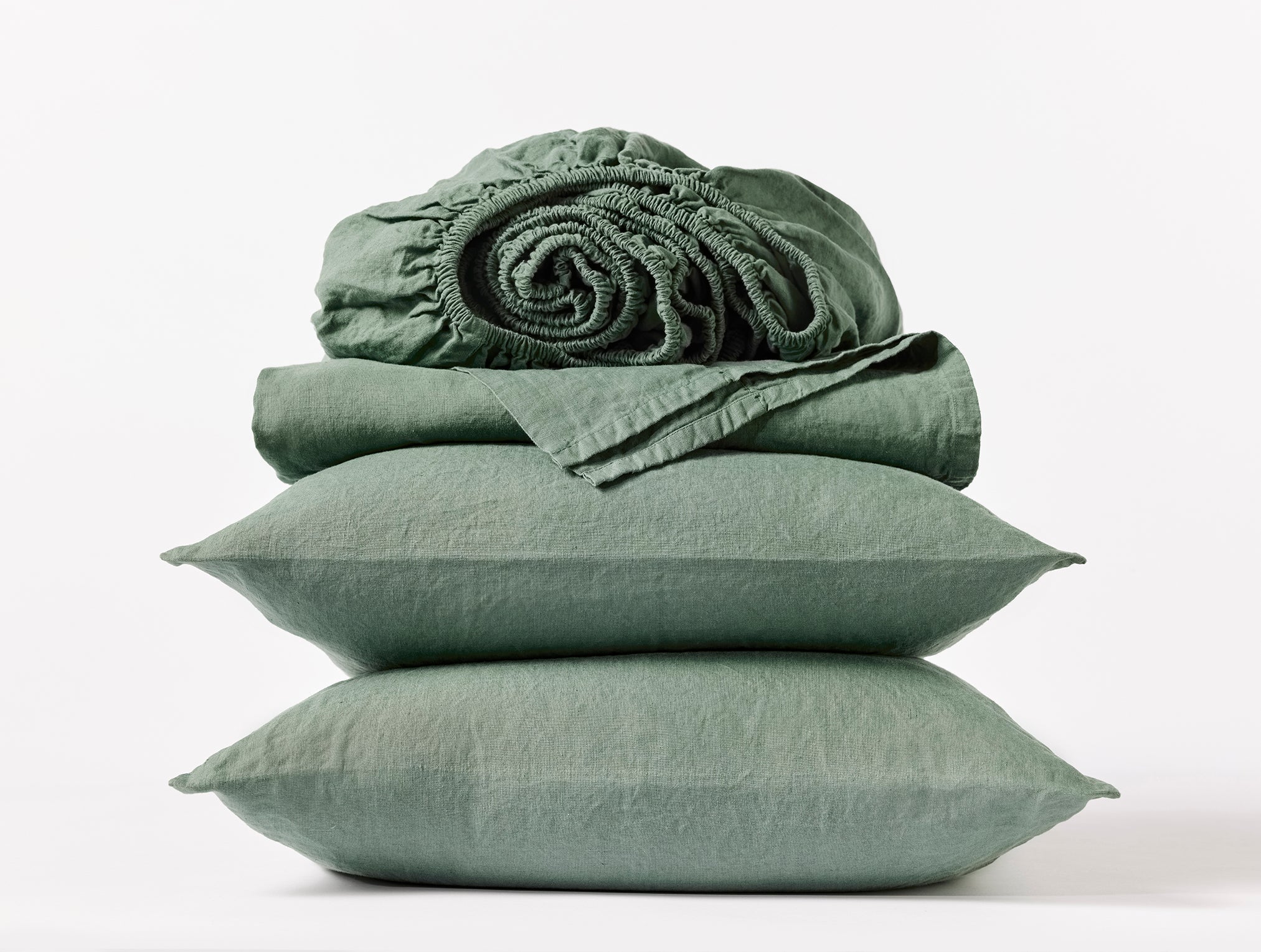 Coyuchi Organic Relaxed Linen Sheet Set in Juniper – stacked display with pillows and folded sheets. #colour_juniper