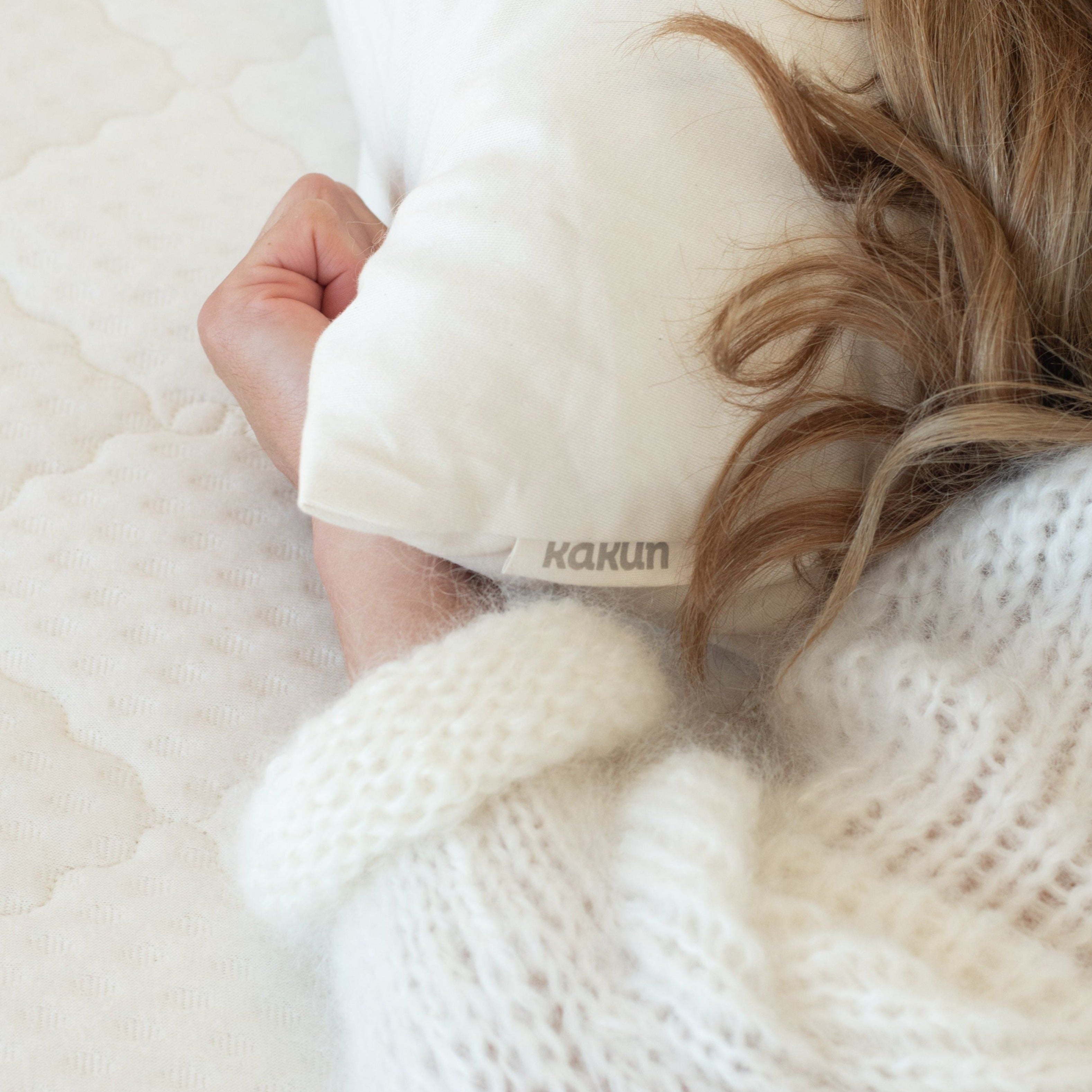 Kakun Organic Wool Pillow - close-up of corner of pillow to show fabric logo tag, with woman laying her head on it.