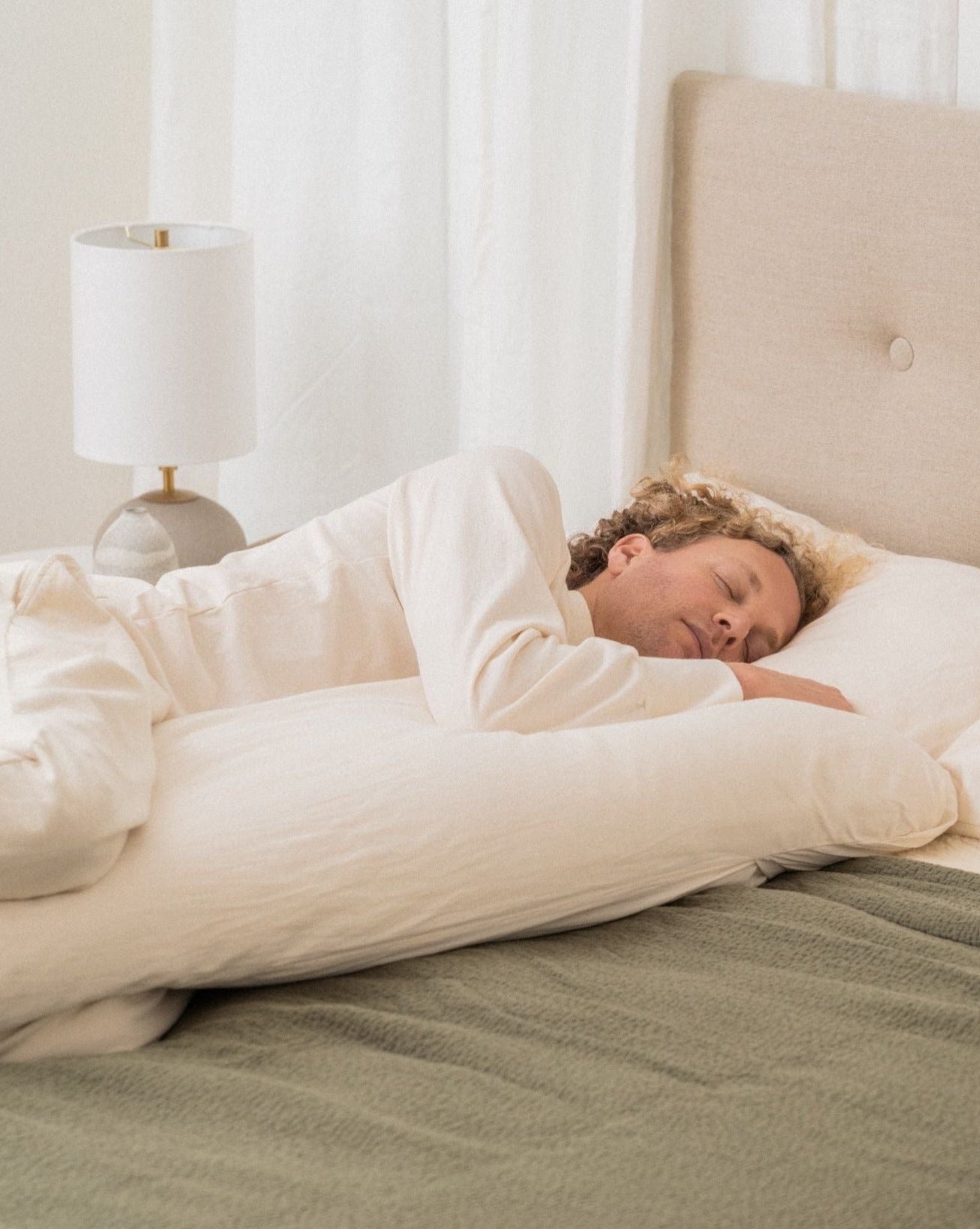 image of a man with curly hair lying on his side showing the organic body pillow supporting his top arm for comfort and alignment