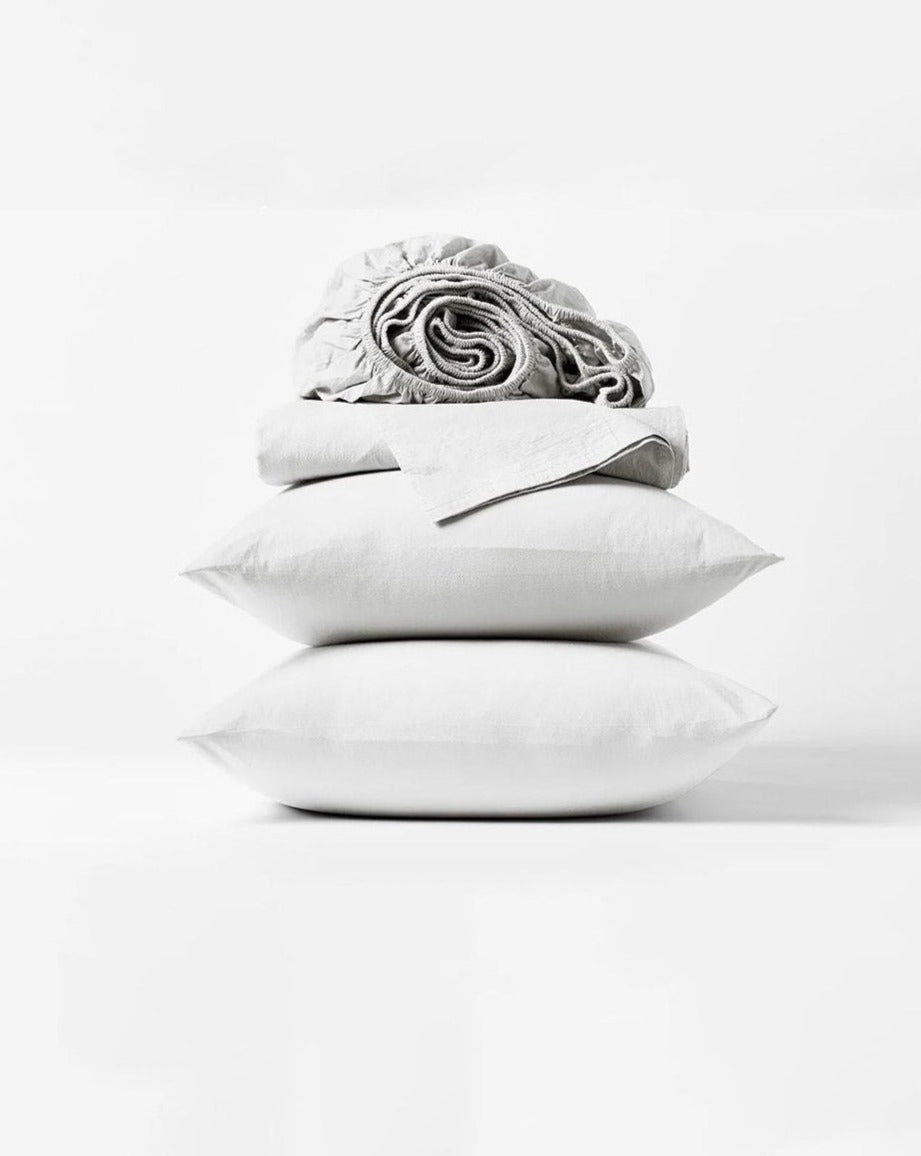 Coyuchi Organic Crinkled Percale Sheet Set in Alpine White – stacked display with pillows and folded sheets. #colour_alpine white