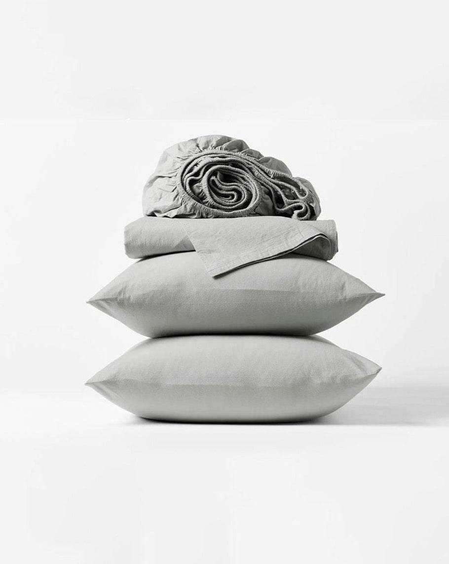 Coyuchi Organic Crinkled Percale Sheet Set in Steel Blue – stacked display with pillows and folded sheets. #colour_pewter