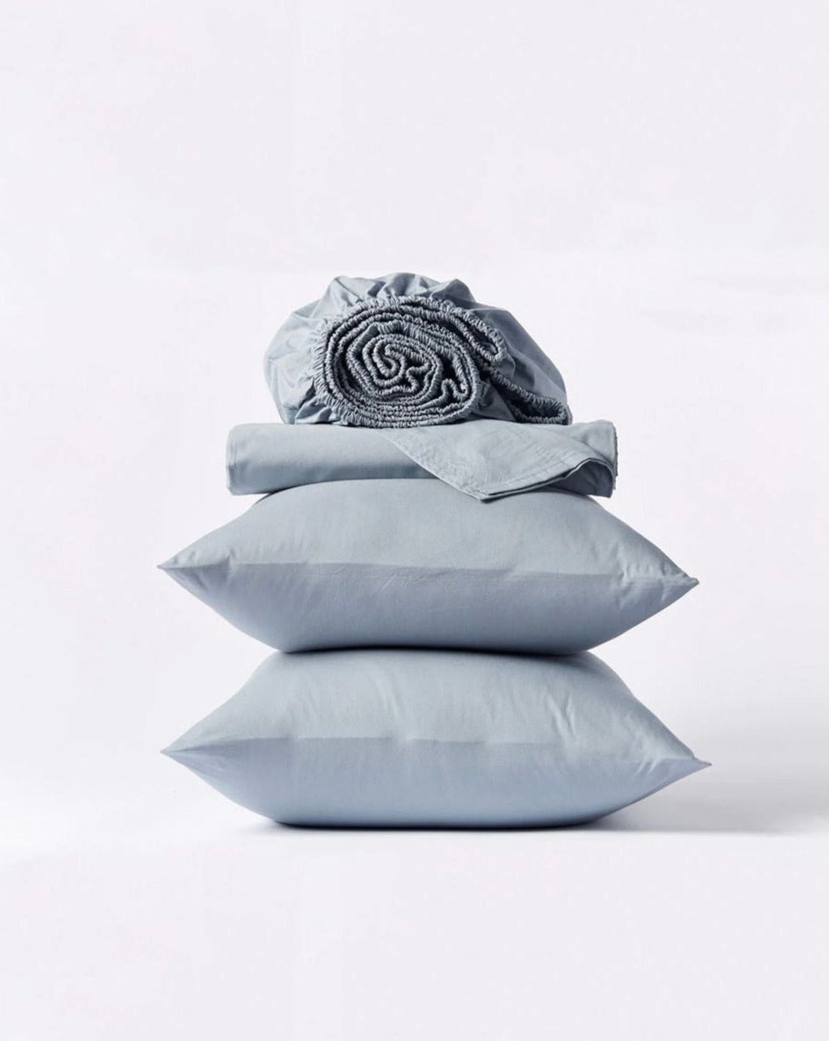 Coyuchi Organic Crinkled Percale Sheet Set in Steel Blue – stacked display with pillows and folded sheets. #colour_steel blue