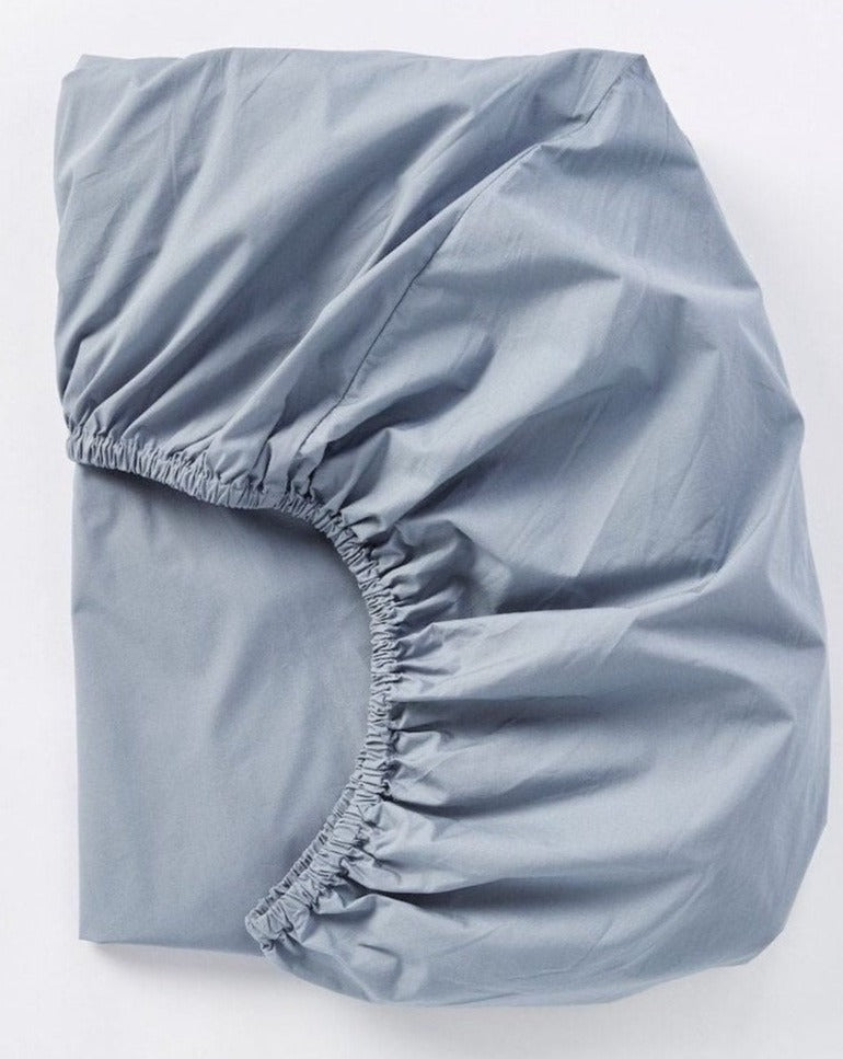 Coyuchi Refined Organic Percale Fitted Sheet in Steel Blue – folded, displaying elastic in seam. #colour_steel blue