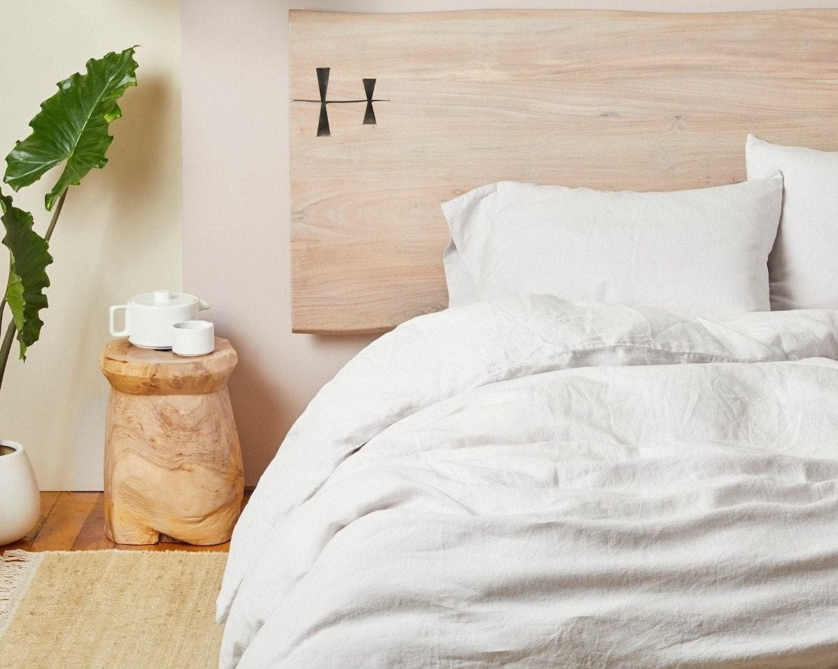 Coyuchi Organic Relaxed Linen Fitted Sheet in Fog – made bed styled with natural wood headboard and side table. #colour_fog