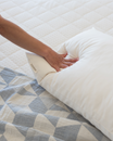 hand pressing on organic kakun pillow lying on blue and grey quilt on an organic mattress