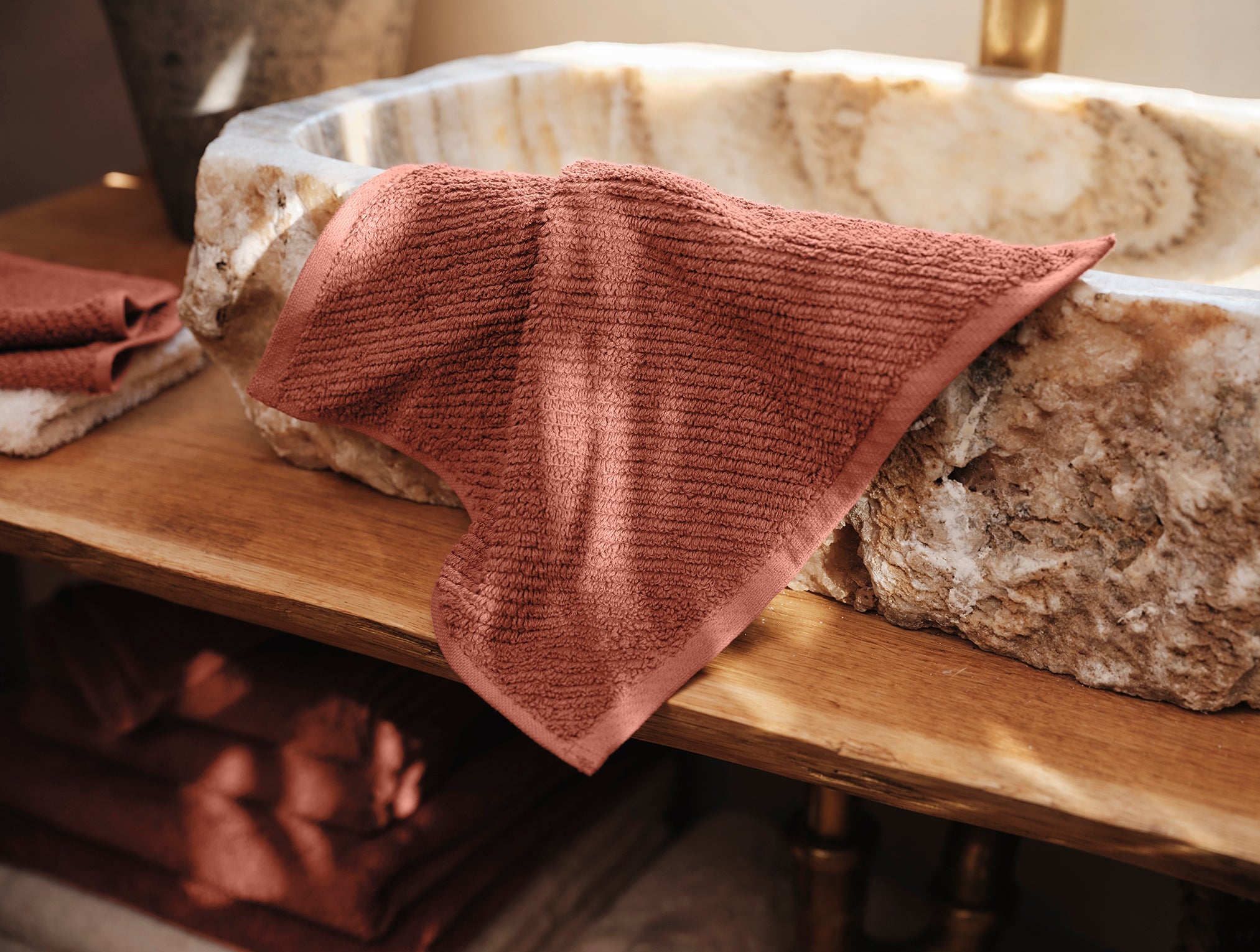 Coyuchi Organic Air Weight Wash Cloth - draped over natural stone sink #color_sedona