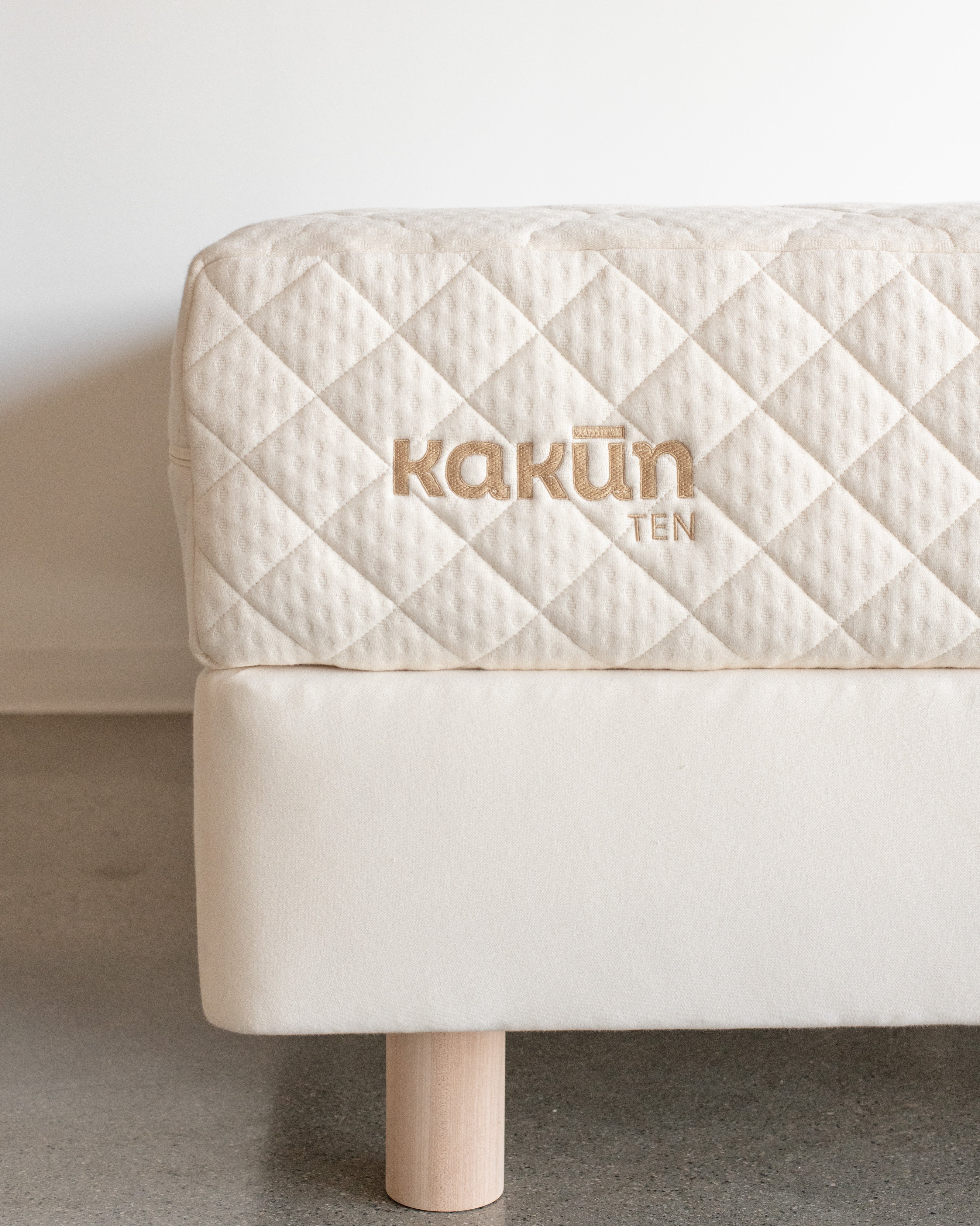 Left corner of the Kakun nine inch organic mattress made in Canada with Kakun logo on an 8 inch Obasan foundation box spring with legs