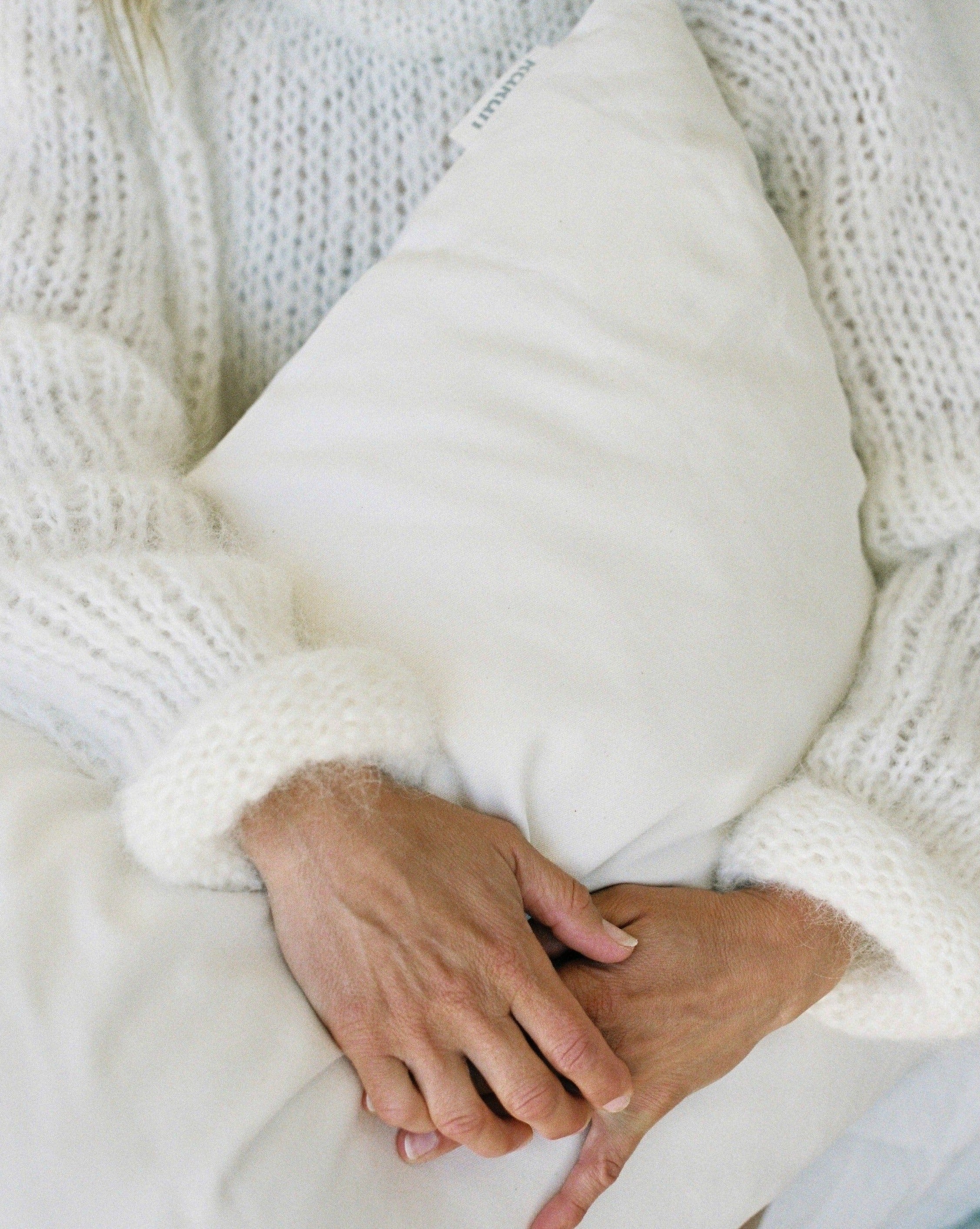 Woman in white knit sweater holding kakun organic wool pllow