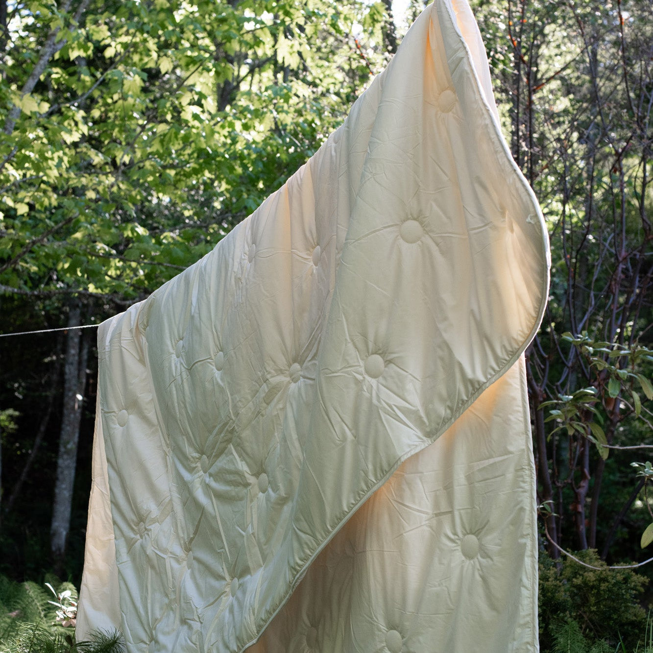 White wool comforter hanging on a clothesline with trees in the background