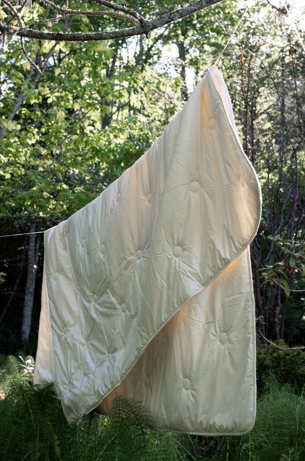Kakun Organic Wool Comforter - hanging in the sunshine on a laundry line, with a forest in the background.
