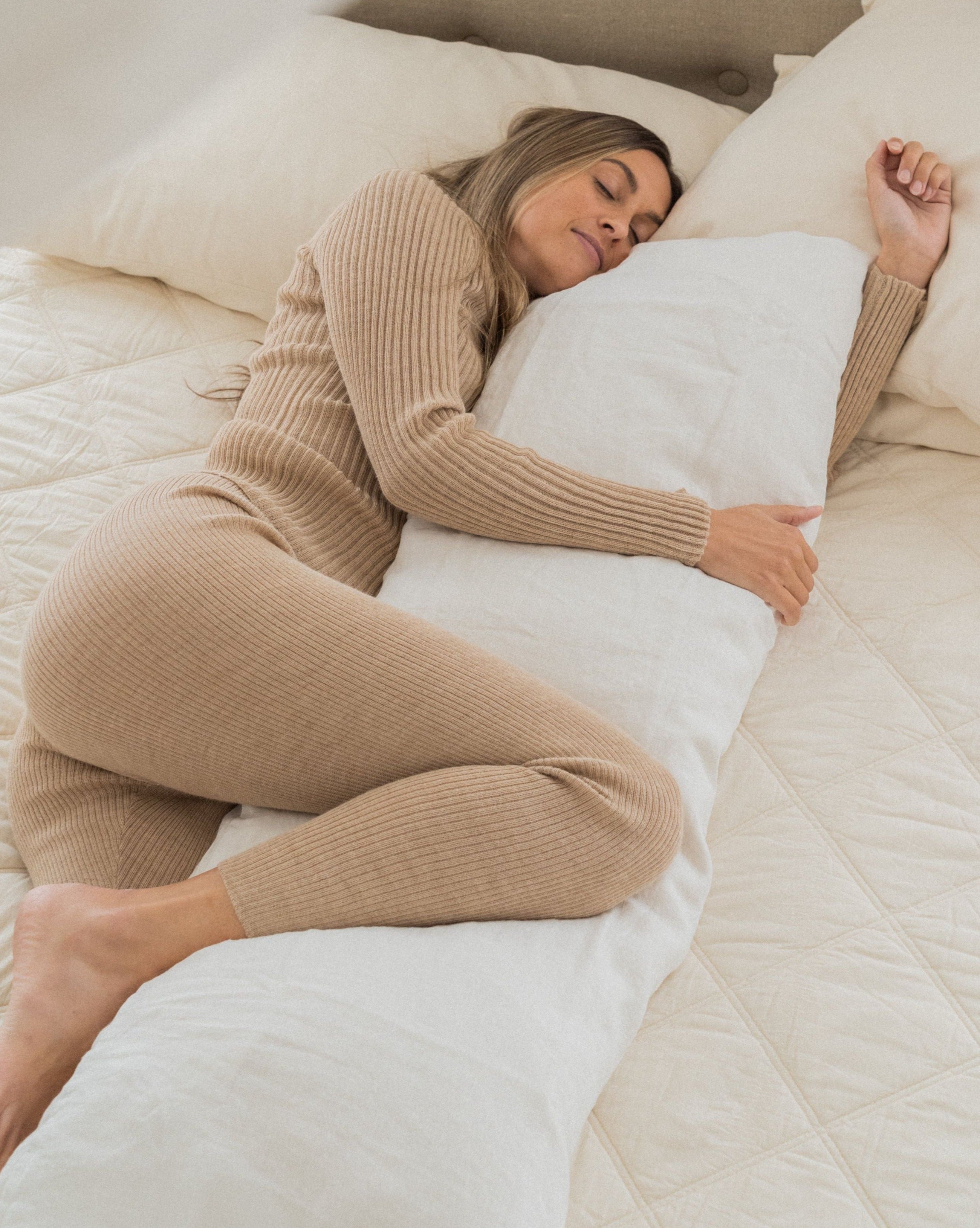image of a woman lying on her side on a bed with her leg and arm supported by a Kakun body pillow