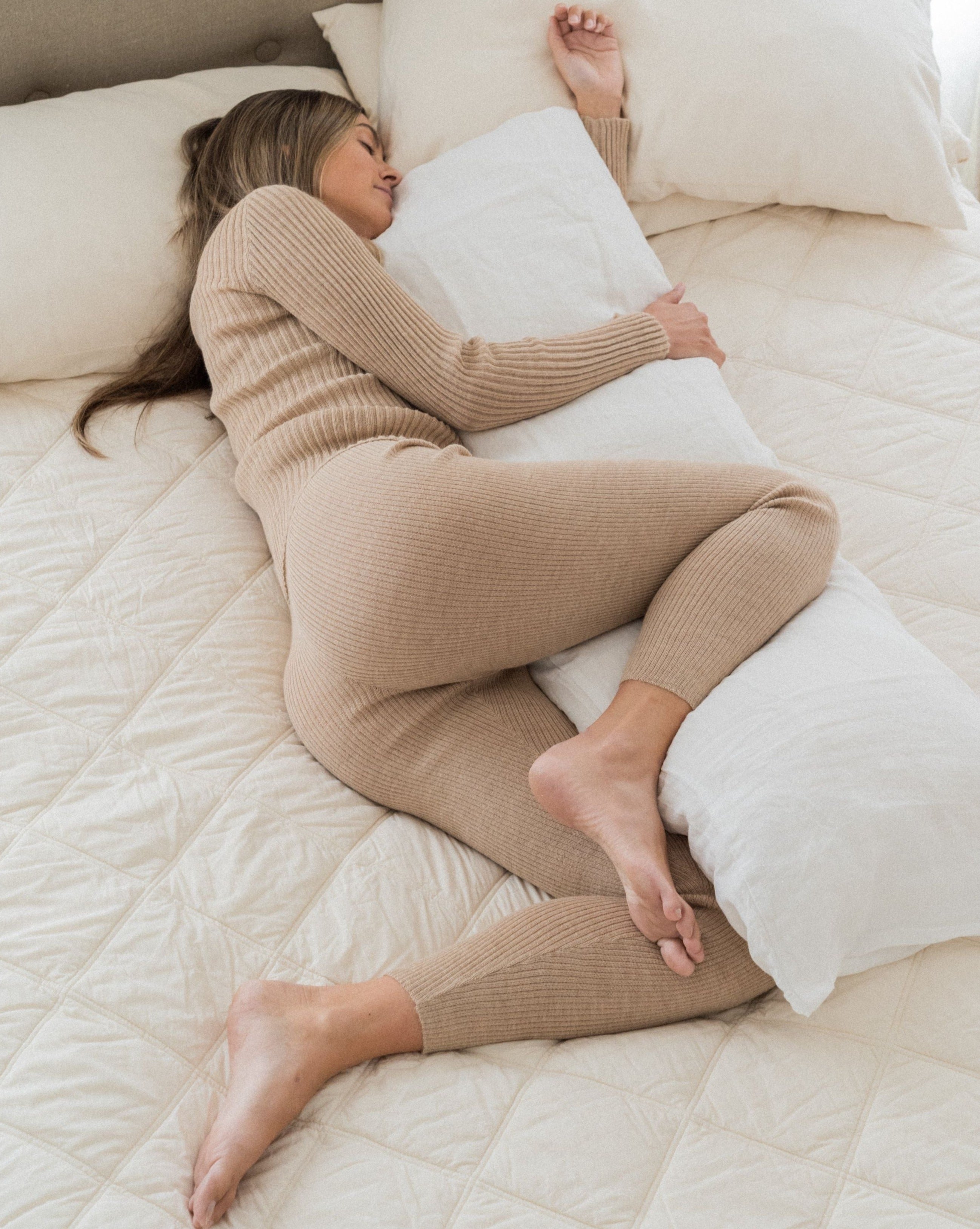 image of woman lying on her side with her top leg and arm supported by an organic wool body pillow
